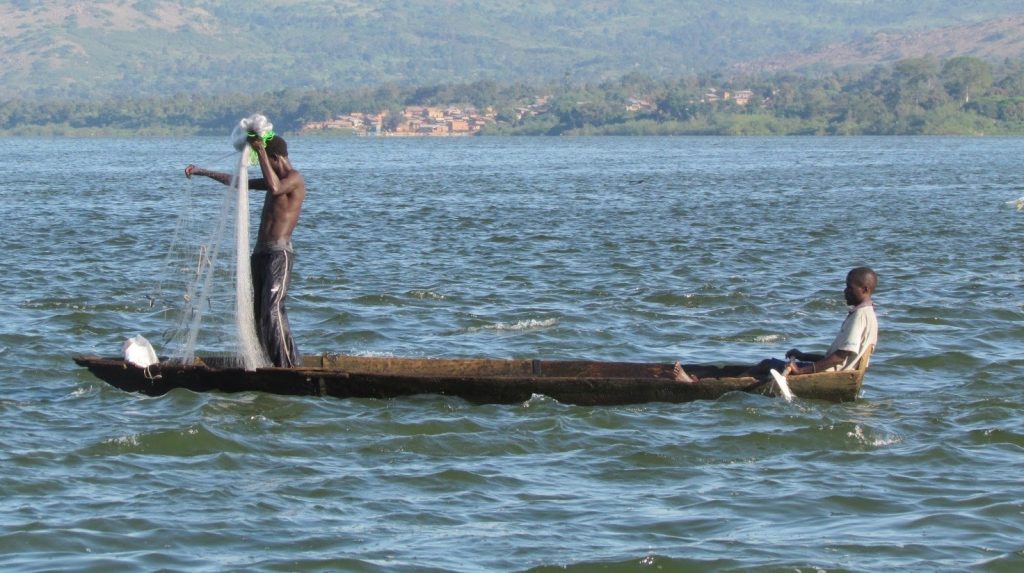 Fishermen casting nets from a canoe on a Ugandan lake